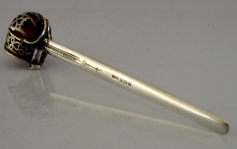An Edwardian sterling silver letter opener featuring a smooth tapered blade stamped with British hallmarks and a decorative pierced finial housing a red orb.