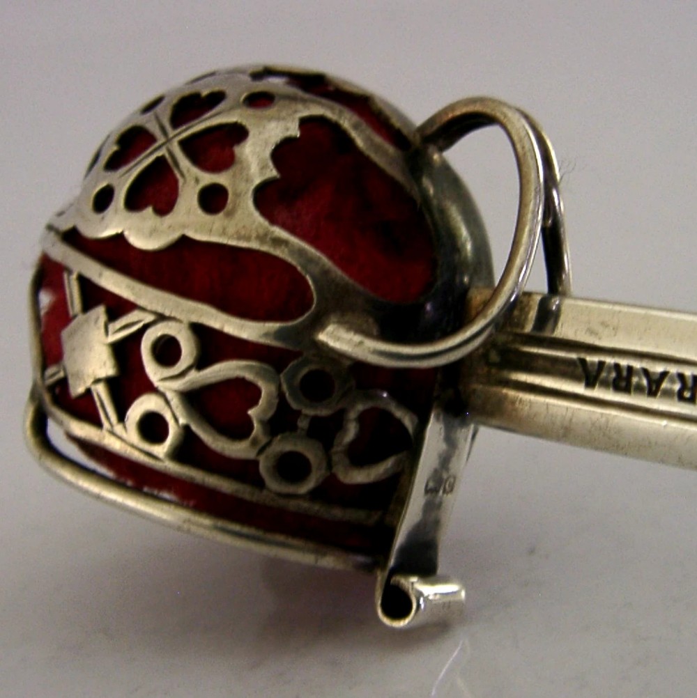 An Edwardian sterling silver letter opener featuring a smooth tapered blade stamped with British hallmarks and a decorative pierced finial housing a red orb. View II