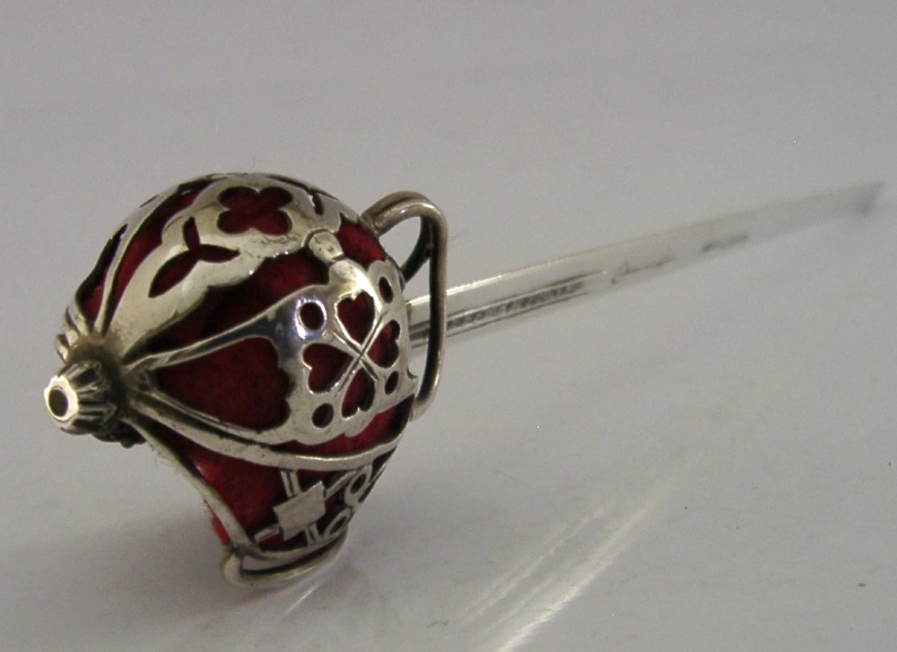 An Edwardian sterling silver letter opener featuring a smooth tapered blade stamped with British hallmarks and a decorative pierced finial housing a red orb. View V