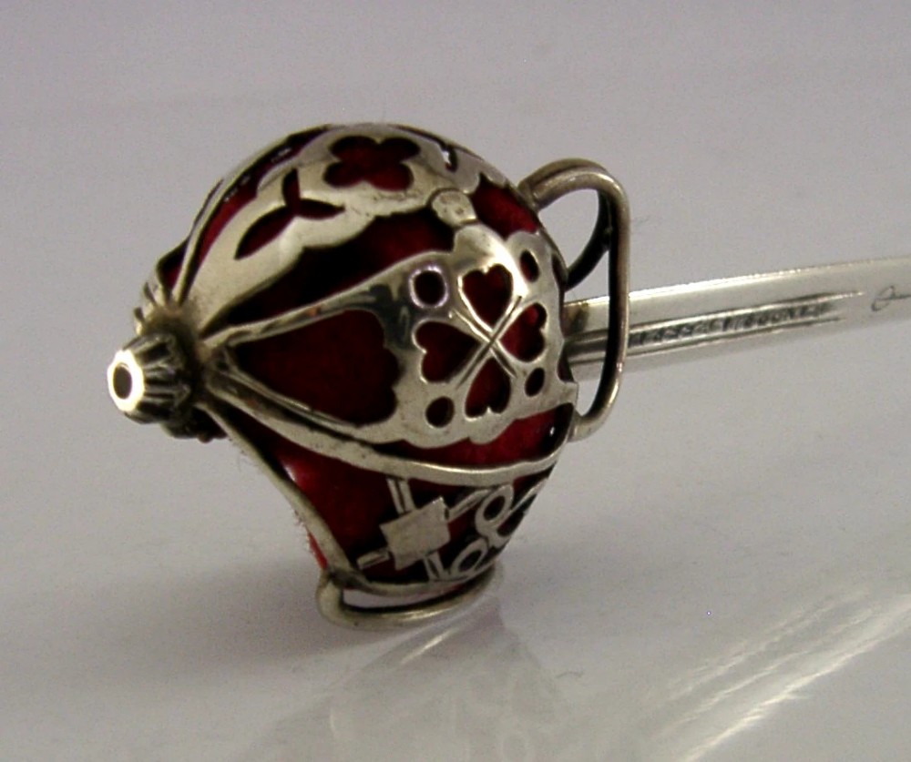 An Edwardian sterling silver letter opener featuring a smooth tapered blade stamped with British hallmarks and a decorative pierced finial housing a red orb. View VI