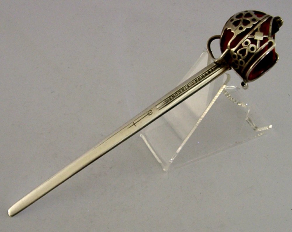 An Edwardian sterling silver letter opener featuring a smooth tapered blade stamped with British hallmarks and a decorative pierced finial housing a red orb. View VII