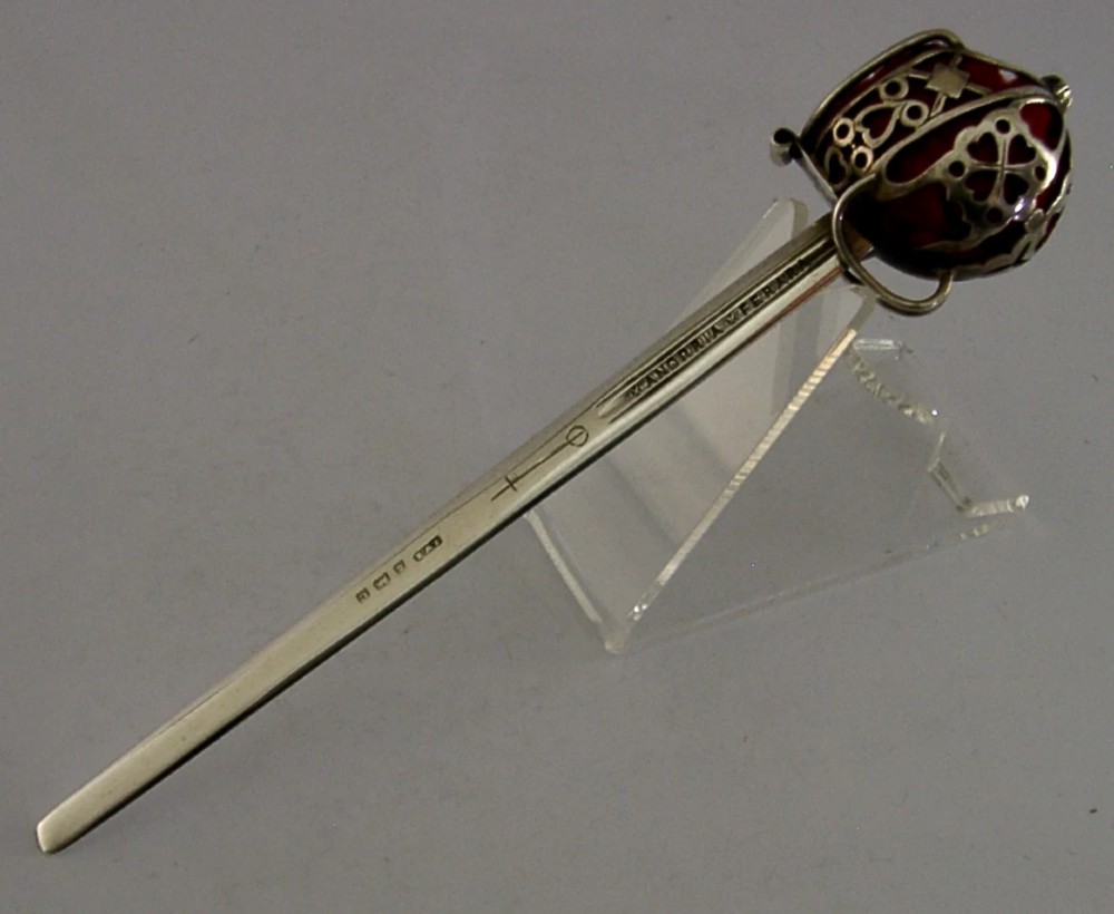 An Edwardian sterling silver letter opener featuring a smooth tapered blade stamped with British hallmarks and a decorative pierced finial housing a red orb. View VIII