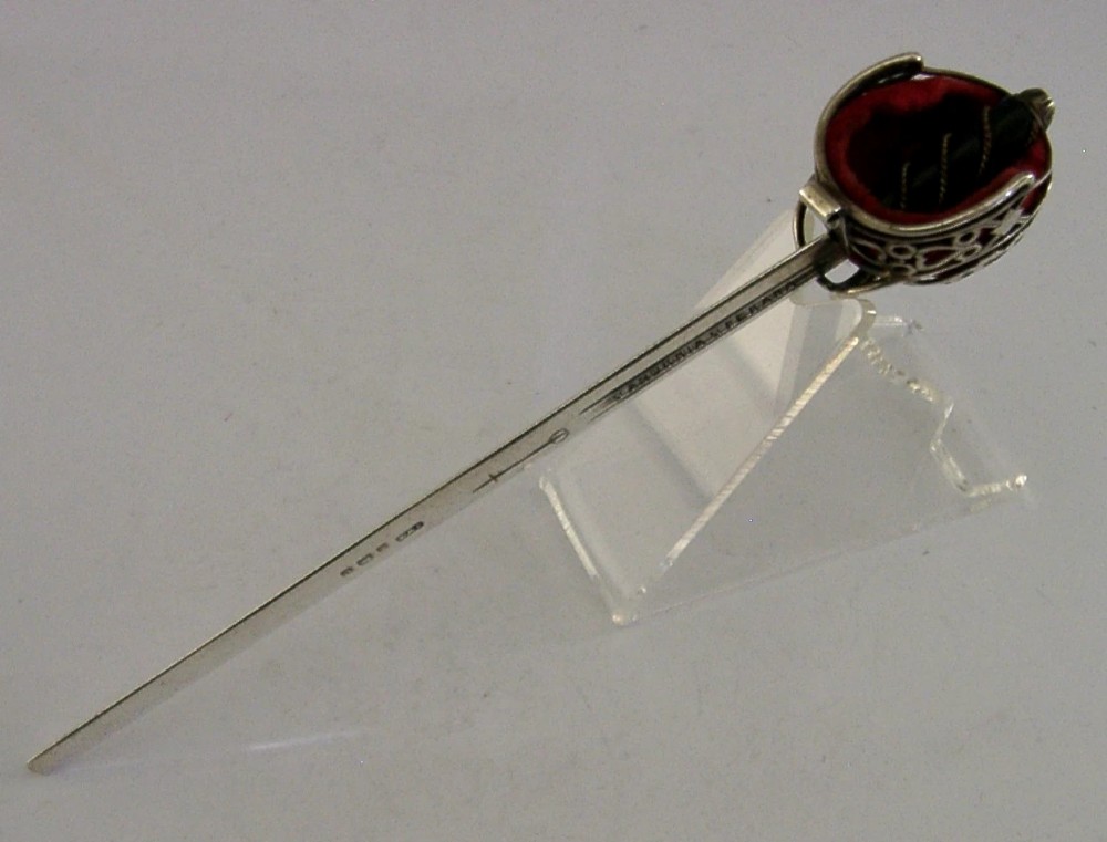 An Edwardian sterling silver letter opener featuring a smooth tapered blade stamped with British hallmarks and a decorative pierced finial housing a red orb. View IX