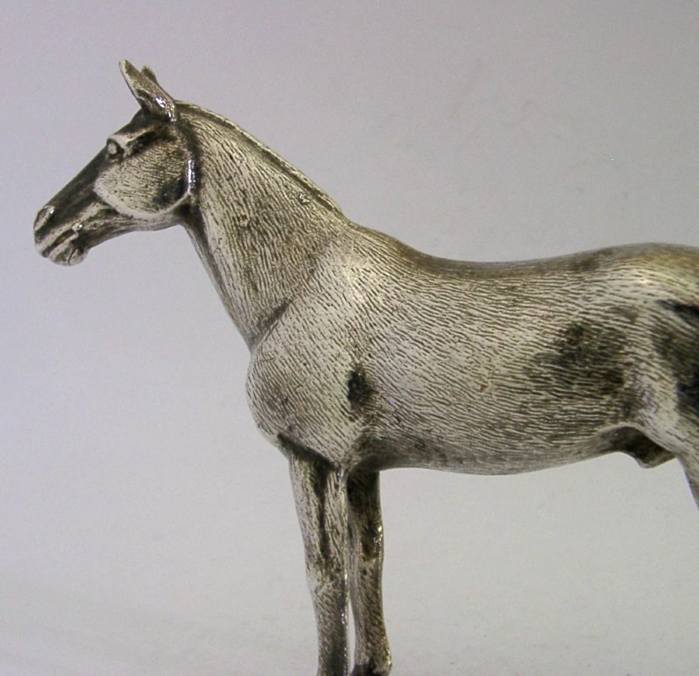 A silver-plated metal figure depicting a standing horse with detailed textured fur, erect ears, and a refined posture. View III