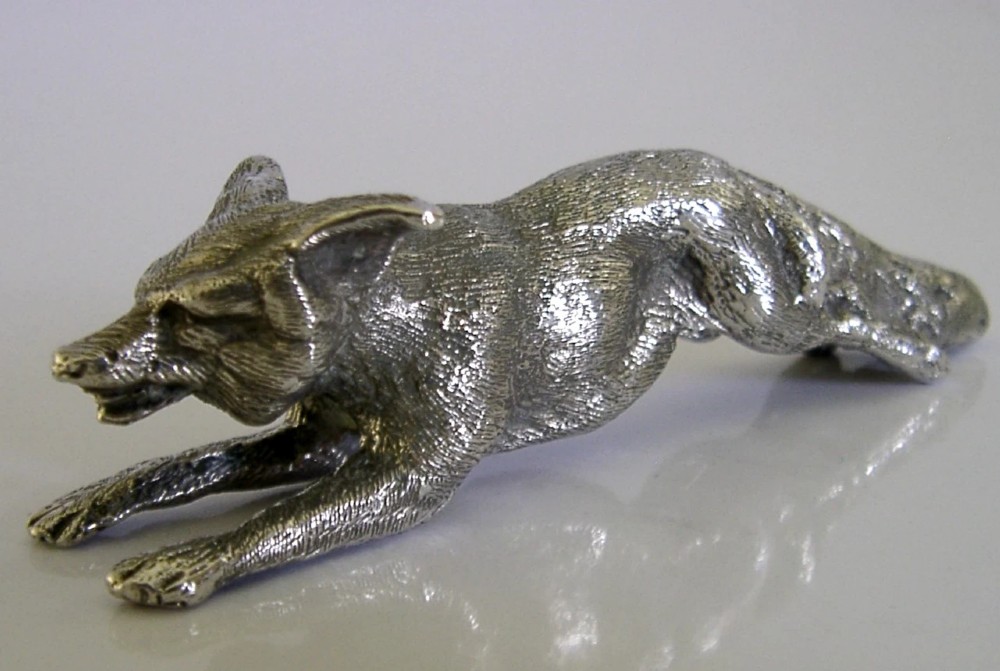 A solid sterling silver figurine depicting a fox in a low running pose with textured fur and detailed features.