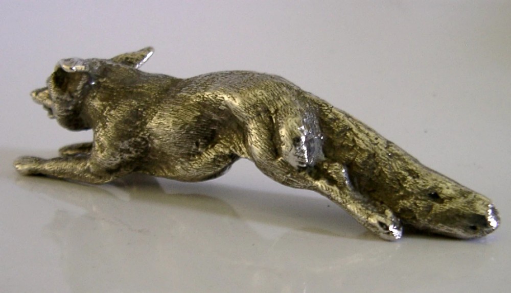 A solid sterling silver figurine depicting a fox in a low running pose with textured fur and detailed features. View IX