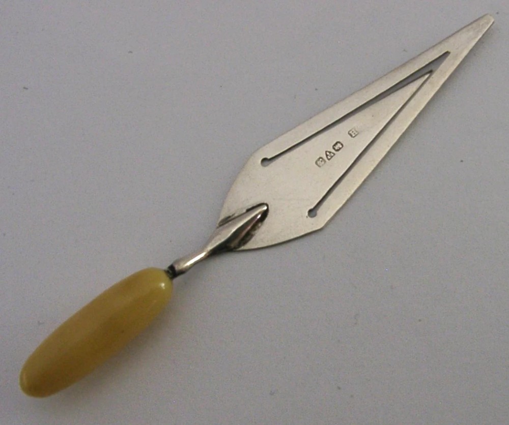 A sterling silver trowel-shaped page marker featuring British hallmarks on the blade and a smooth, rounded yellow handle.