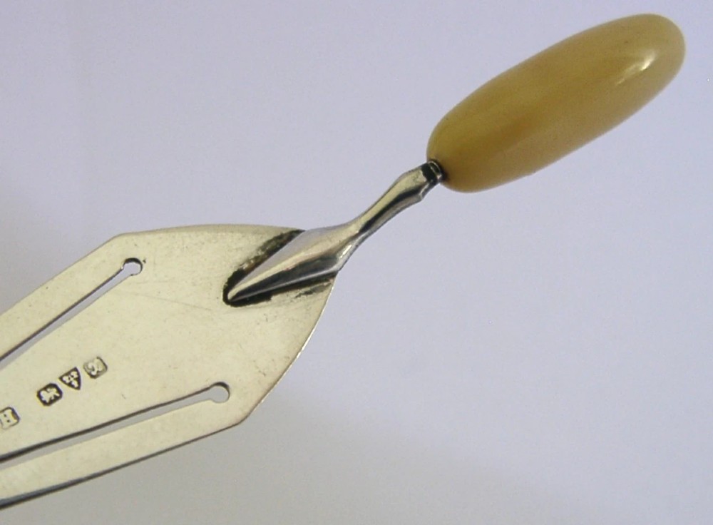 A sterling silver trowel-shaped page marker featuring British hallmarks on the blade and a smooth, rounded yellow handle. View II