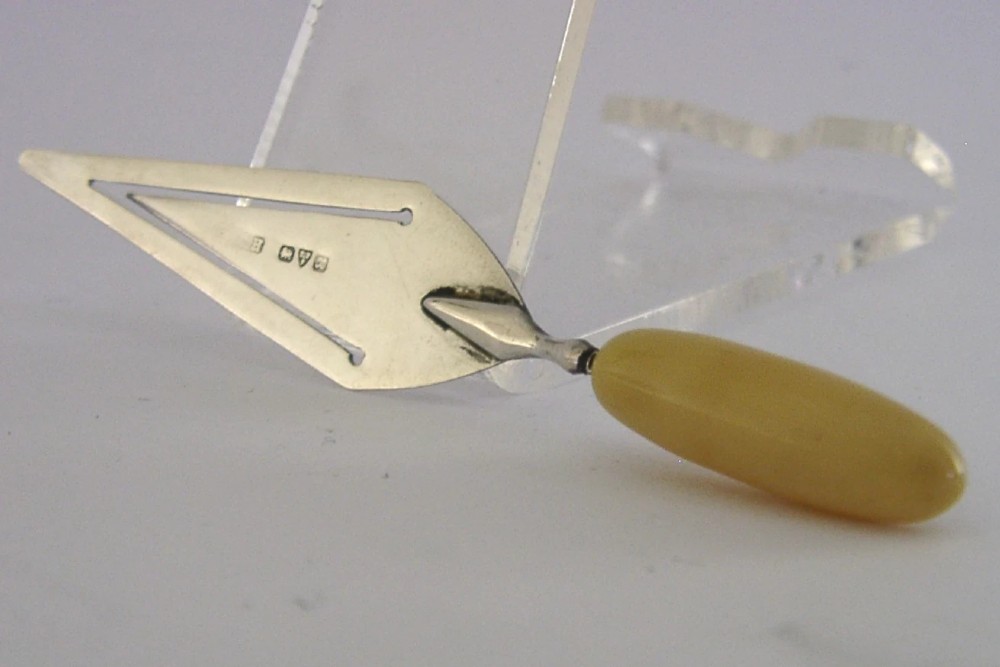 A sterling silver trowel-shaped page marker featuring British hallmarks on the blade and a smooth, rounded yellow handle. View III