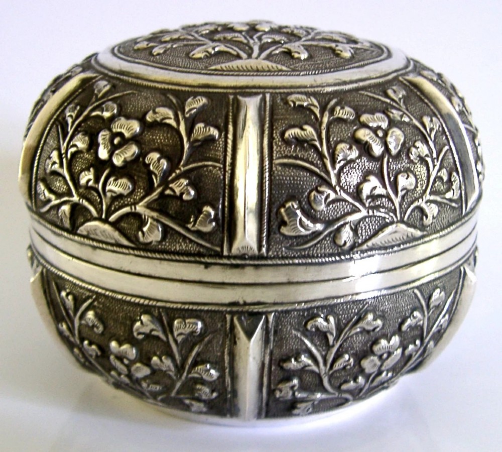 A circular antique solid silver export box decorated with hand-chased floral motifs and a stippled textured background. View II