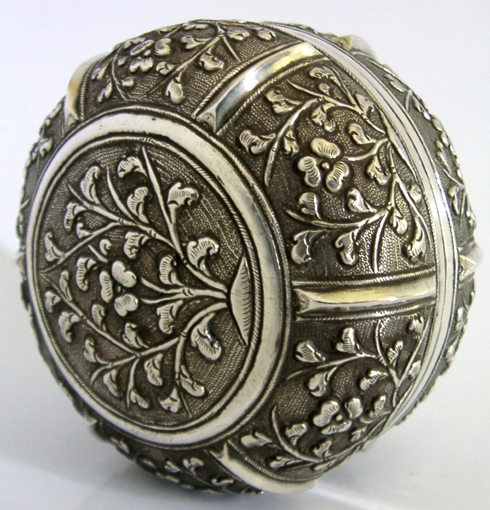 A circular antique solid silver export box decorated with hand-chased floral motifs and a stippled textured background.