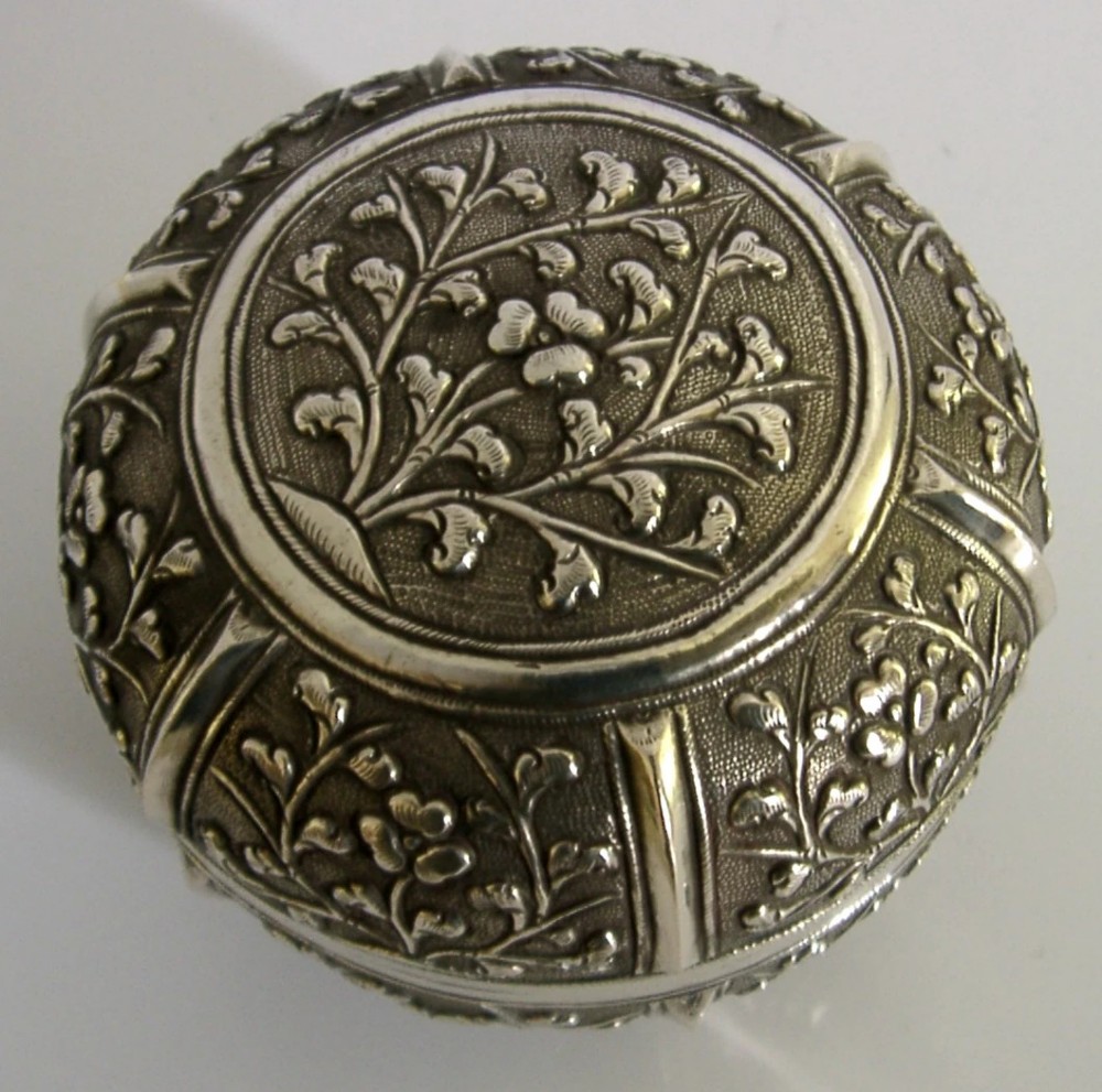 A circular antique solid silver export box decorated with hand-chased floral motifs and a stippled textured background. View III