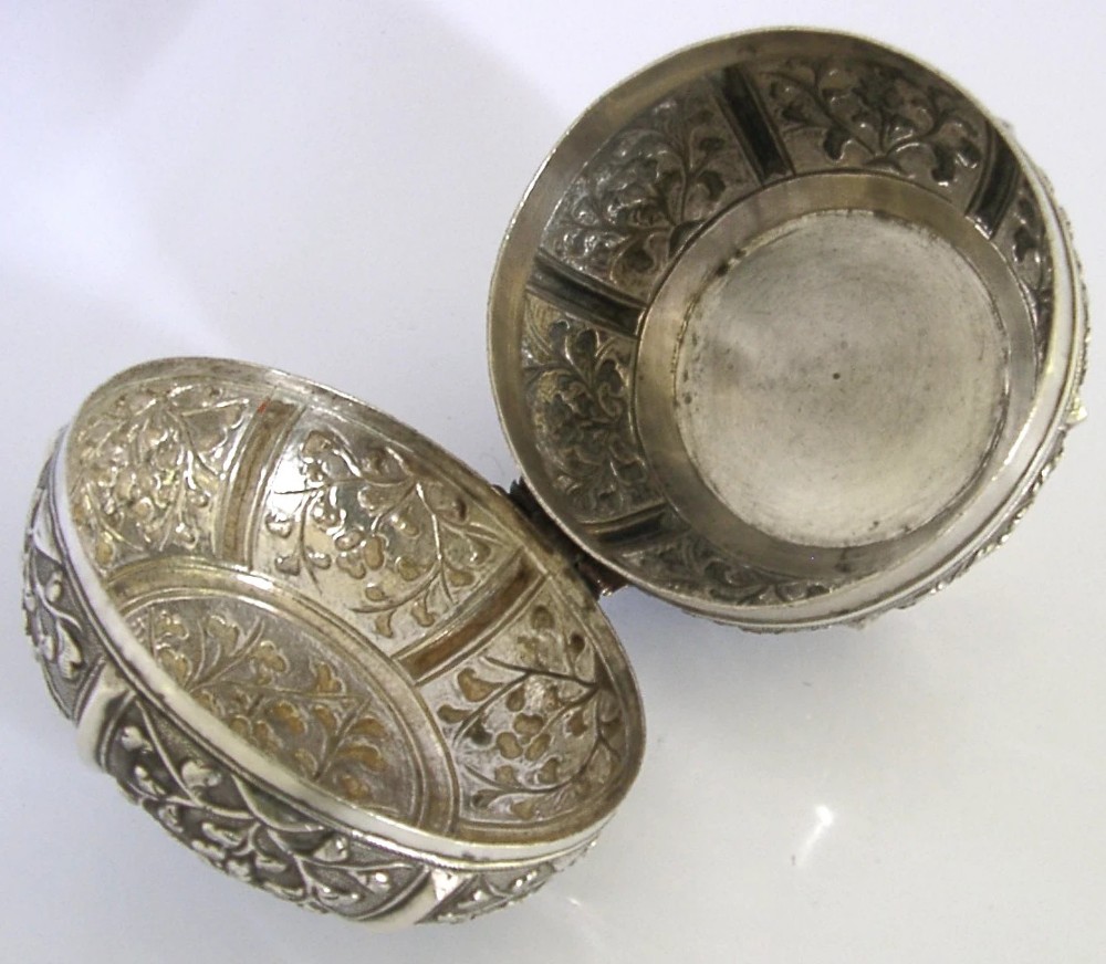 A circular antique solid silver export box decorated with hand-chased floral motifs and a stippled textured background. View V