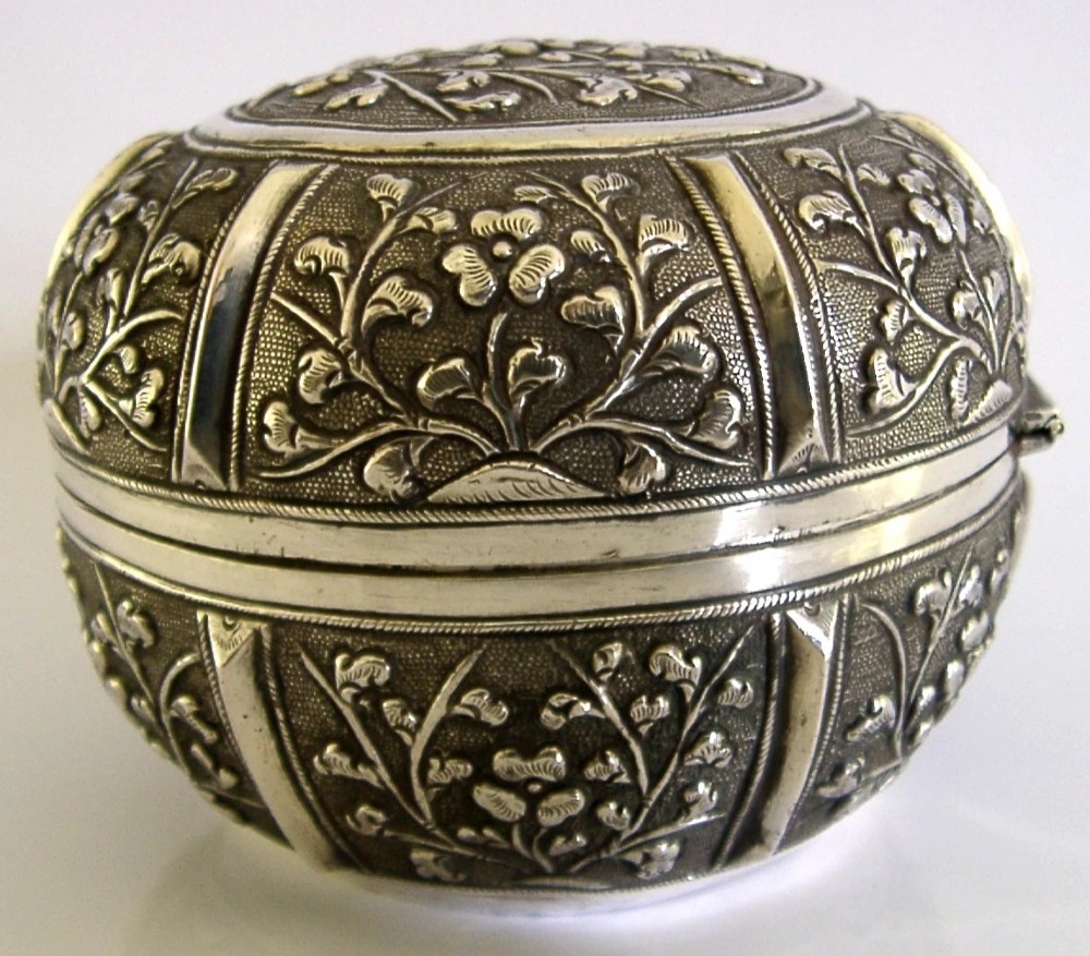 A circular antique solid silver export box decorated with hand-chased floral motifs and a stippled textured background. View VI