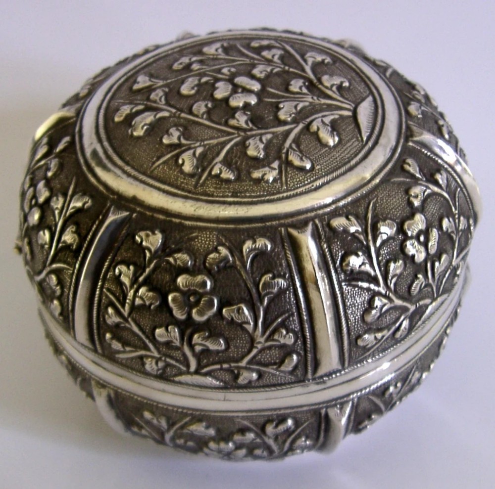 A circular antique solid silver export box decorated with hand-chased floral motifs and a stippled textured background. View VII