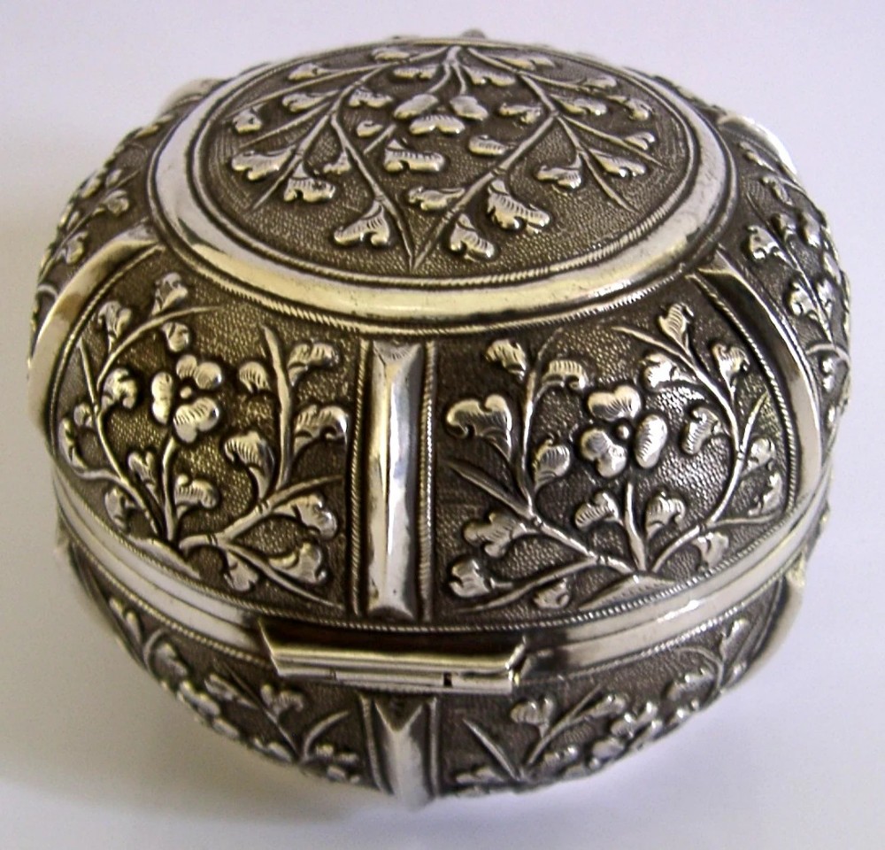 A circular antique solid silver export box decorated with hand-chased floral motifs and a stippled textured background. View IX