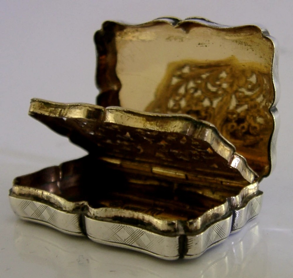 An open Victorian sterling silver vinaigrette box by Nathaniel Mills featuring a scalloped edge, cross-hatch engraving, and an internal hinged pierced gilt grill.