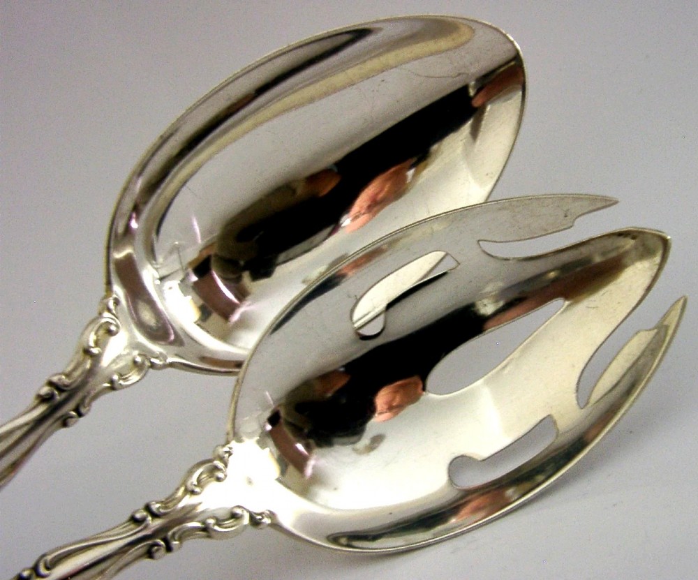 A pair of late Victorian solid sterling silver salad servers featuring ornate scroll edging and a pierced fork head alongside a matching spoon. View II