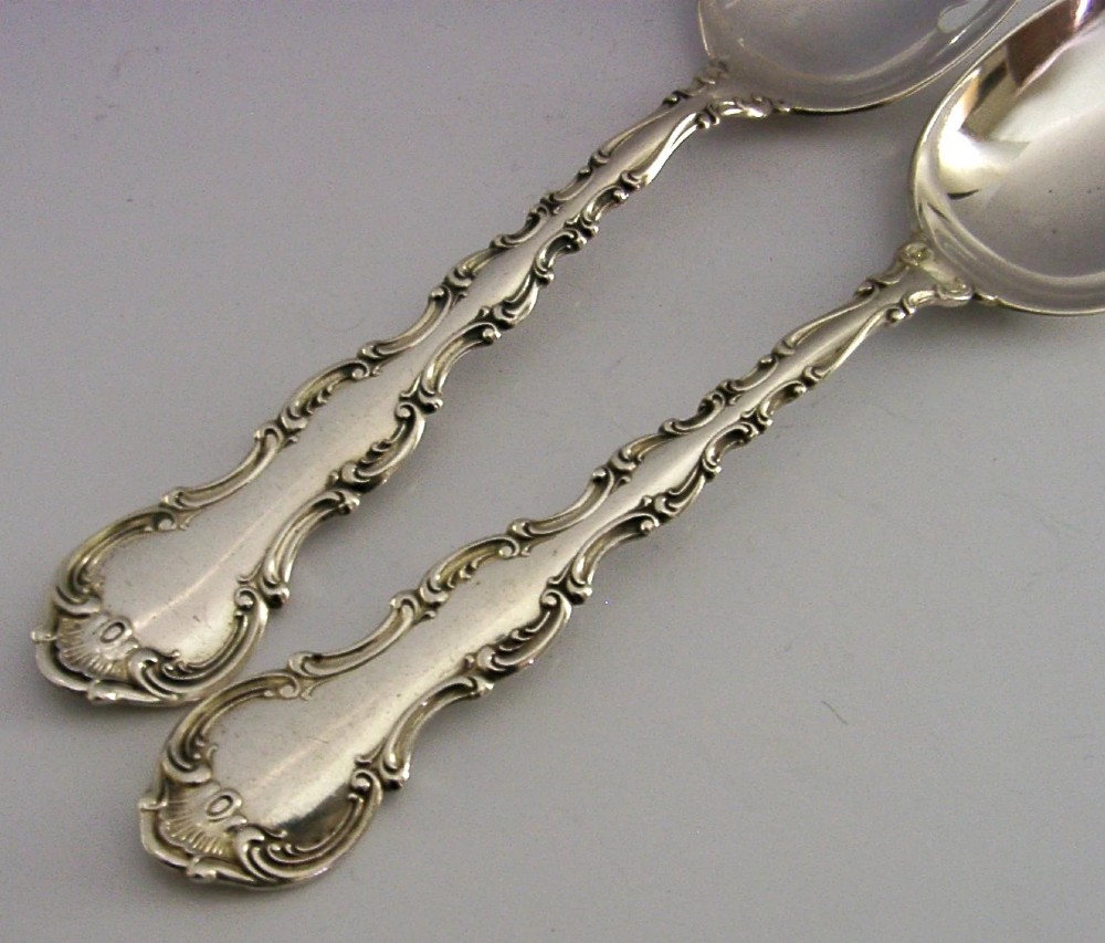 A pair of late Victorian solid sterling silver salad servers featuring ornate scroll edging and a pierced fork head alongside a matching spoon. View V