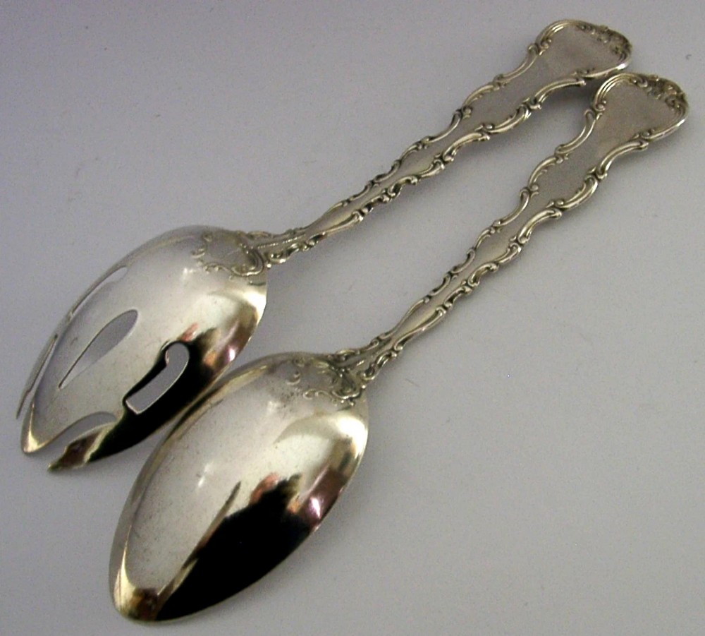 A pair of late Victorian solid sterling silver salad servers featuring ornate scroll edging and a pierced fork head alongside a matching spoon. View VI