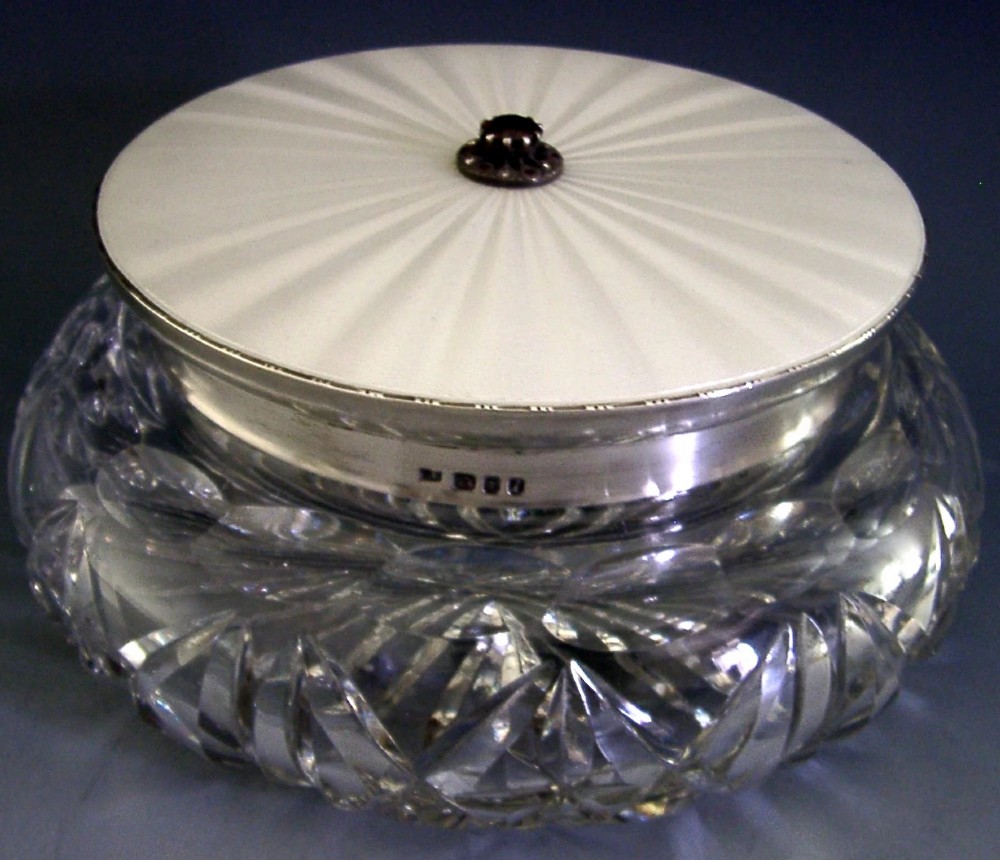 A circular cut glass dressing table jar topped with a white guilloche enamel and sterling silver lid. View V