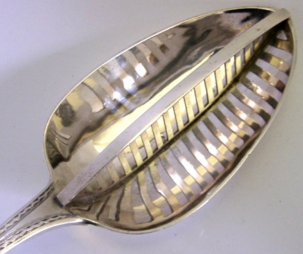 A Georgian sterling silver basting spoon with a Celtic point handle featuring bright-cut engraving and a slatted strainer divider inside the bowl. View II