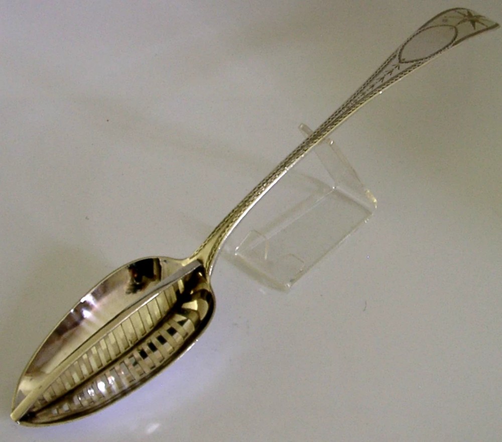 A Georgian sterling silver basting spoon with a Celtic point handle featuring bright-cut engraving and a slatted strainer divider inside the bowl. View III