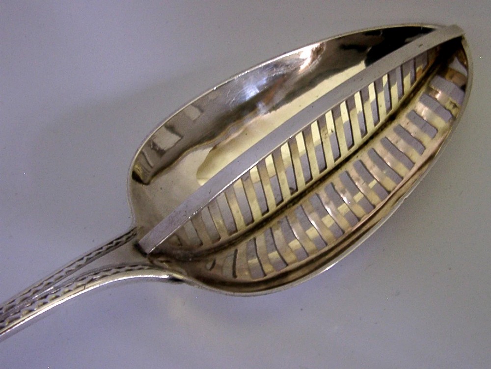 A Georgian sterling silver basting spoon with a Celtic point handle featuring bright-cut engraving and a slatted strainer divider inside the bowl. View IV
