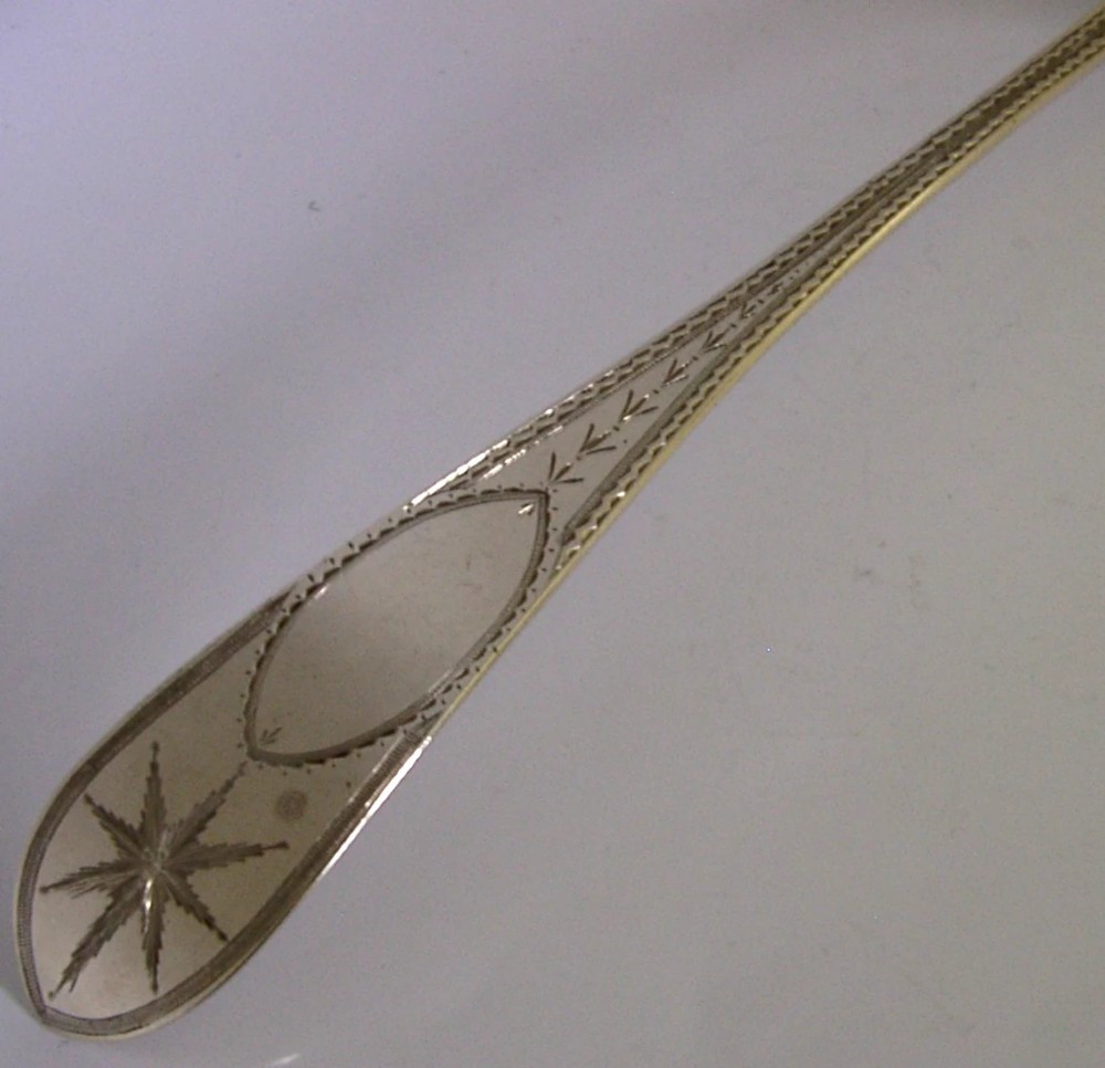 A Georgian sterling silver basting spoon with a Celtic point handle featuring bright-cut engraving and a slatted strainer divider inside the bowl. View V