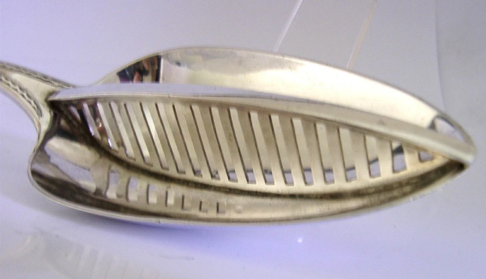 A Georgian sterling silver basting spoon with a Celtic point handle featuring bright-cut engraving and a slatted strainer divider inside the bowl. View VI