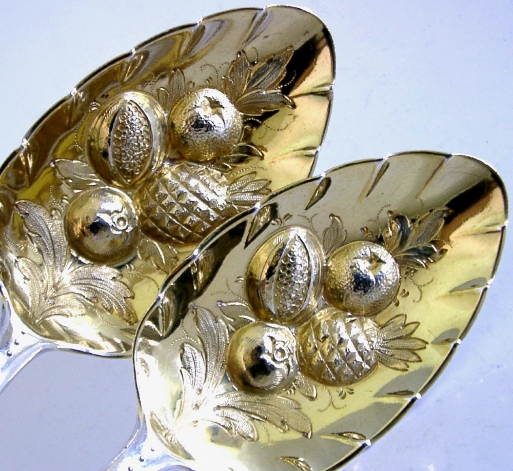 A pair of 1815 Georgian sterling silver berry spoons featuring scroll-engraved handles with family crests and gilt bowls embossed with fruit motifs. View II