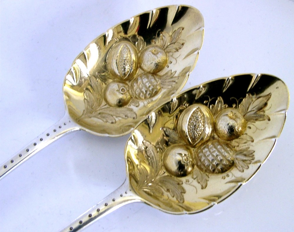 A pair of 1815 Georgian sterling silver berry spoons featuring scroll-engraved handles with family crests and gilt bowls embossed with fruit motifs. View IV