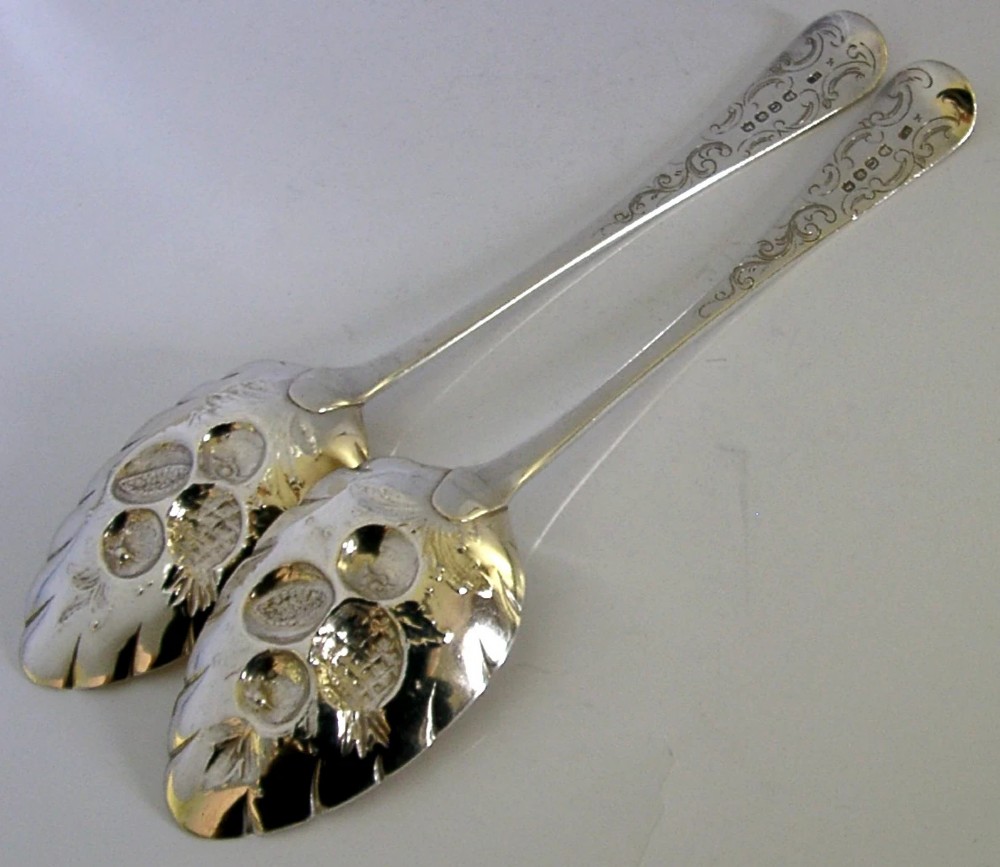 A pair of 1815 Georgian sterling silver berry spoons featuring scroll-engraved handles with family crests and gilt bowls embossed with fruit motifs. View V