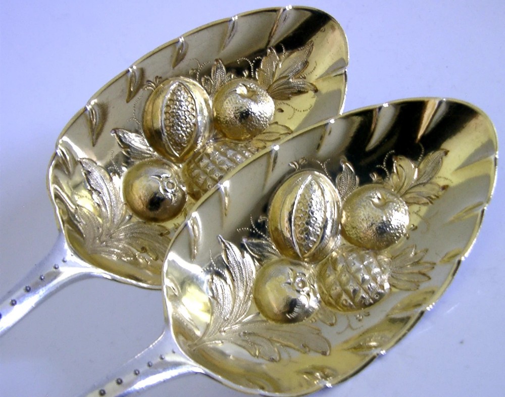 A pair of 1815 Georgian sterling silver berry spoons featuring scroll-engraved handles with family crests and gilt bowls embossed with fruit motifs. View VI