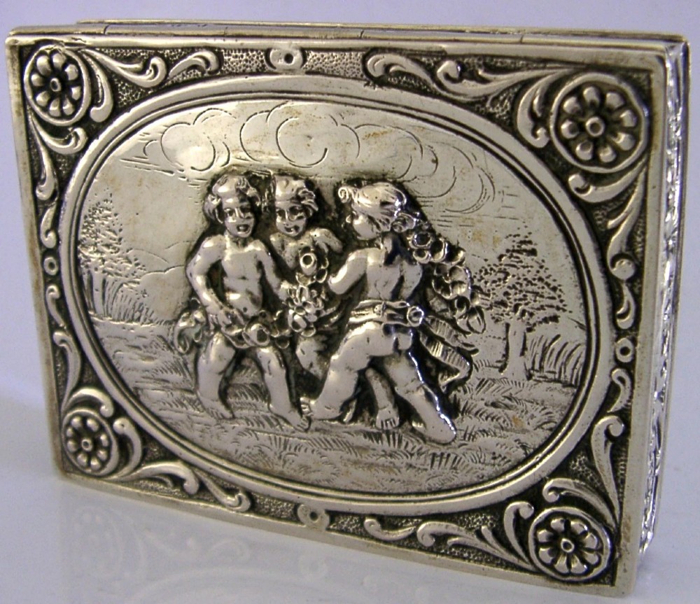 A rectangular silver trinket box featuring an embossed relief scene of three cherubs inside an oval medallion on the hinged lid.