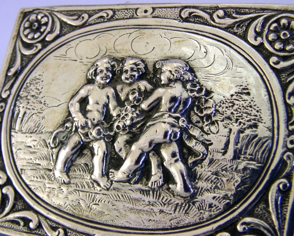A rectangular silver trinket box featuring an embossed relief scene of three cherubs inside an oval medallion on the hinged lid. View II