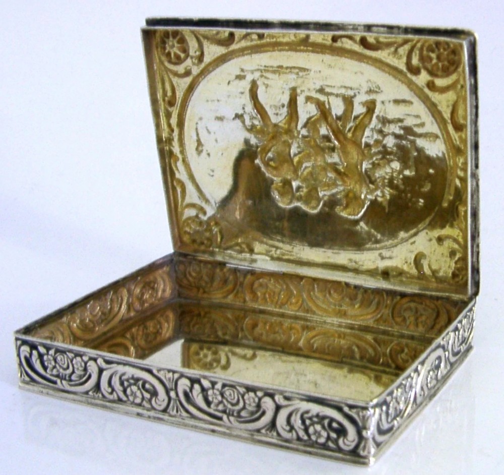A rectangular silver trinket box featuring an embossed relief scene of three cherubs inside an oval medallion on the hinged lid. View VI