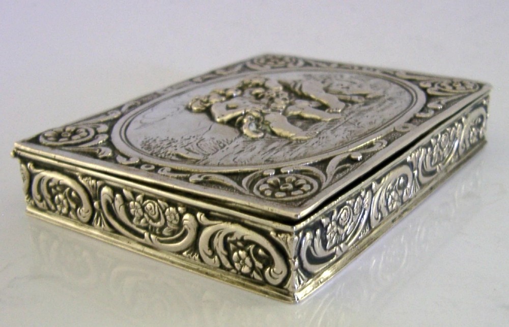 A rectangular silver trinket box featuring an embossed relief scene of three cherubs inside an oval medallion on the hinged lid. View VIII