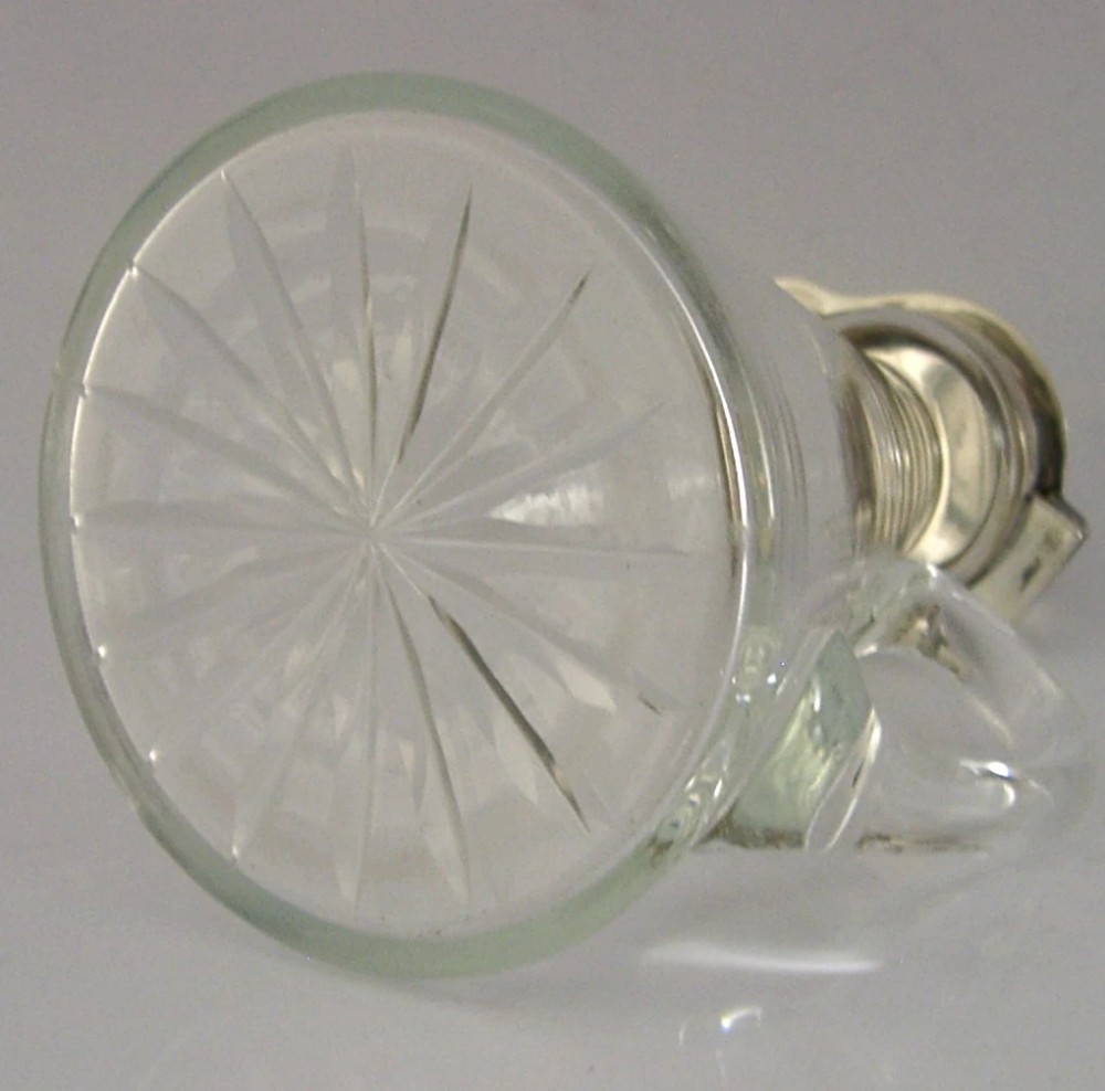 A conical clear glass mini whisky decanter featuring a silver hinged lid with British hallmarks, a side handle, and a star-cut base. View V