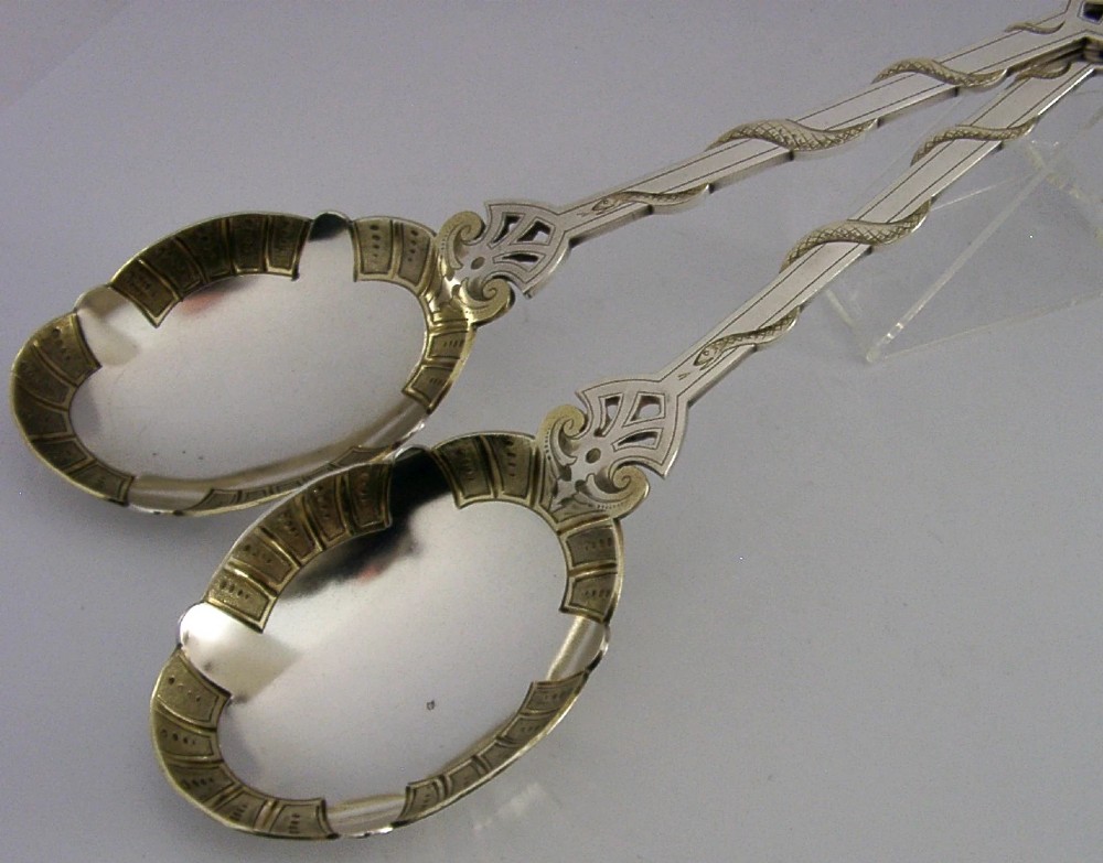 A pair of Victorian silver-plated serving spoons featuring handles entwined with relief-moulded snakes and engraved oval bowls with gilded borders.