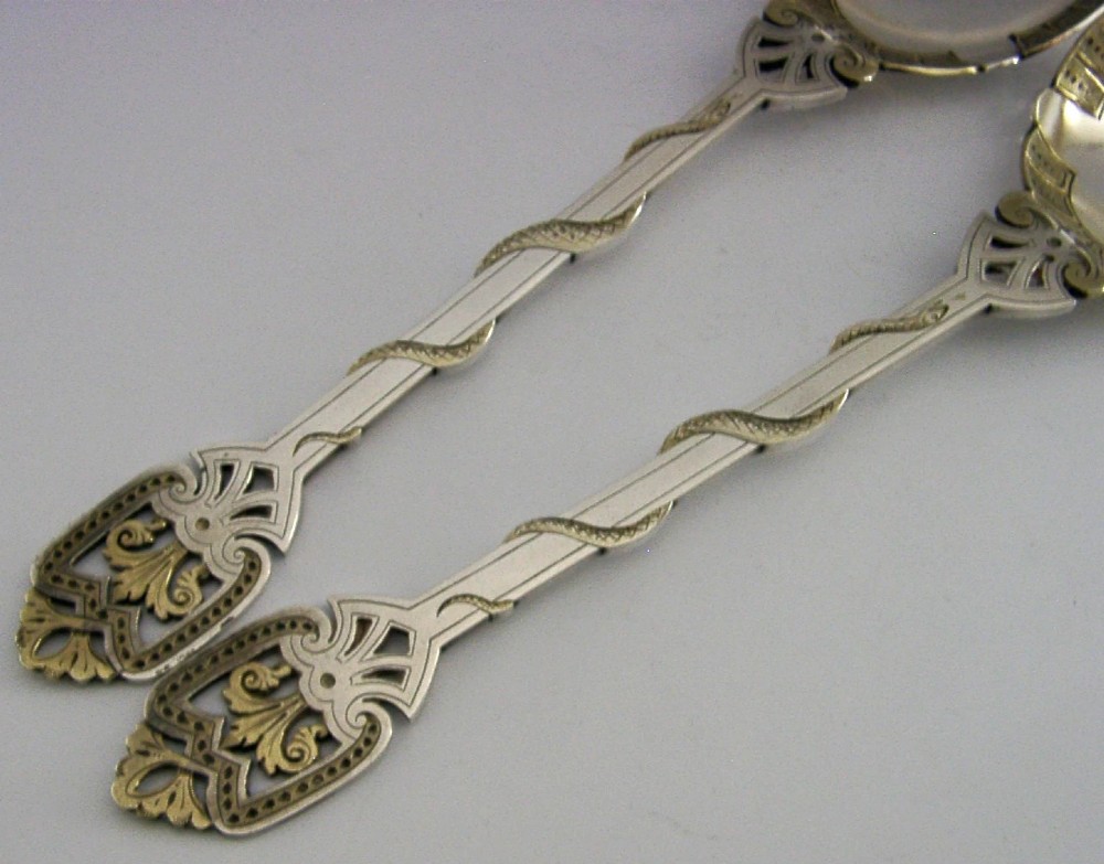 A pair of Victorian silver-plated serving spoons featuring handles entwined with relief-moulded snakes and engraved oval bowls with gilded borders. View V