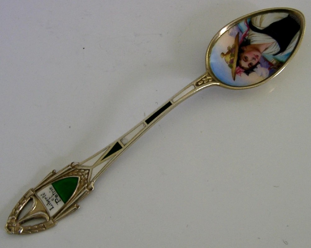 An antique solid silver souvenir spoon featuring a hand-painted enamelled bowl depicting a portrait of a Swiss woman in traditional attire, complete with a green enamelled handle terminal.