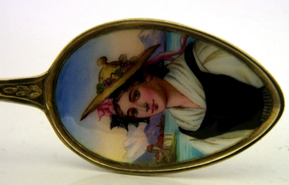 An antique solid silver souvenir spoon featuring a hand-painted enamelled bowl depicting a portrait of a Swiss woman in traditional attire, complete with a green enamelled handle terminal. View V