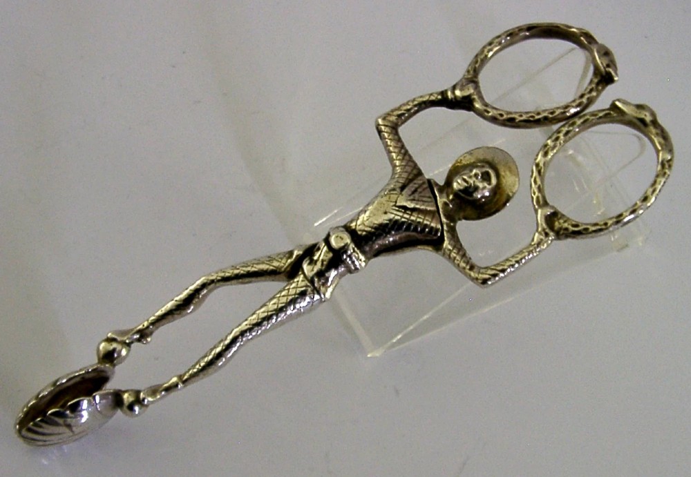 An Edwardian sterling silver sugar nip designed in the detailed shape of a harlequin jester with scissor-action handles and shell-shaped grips.