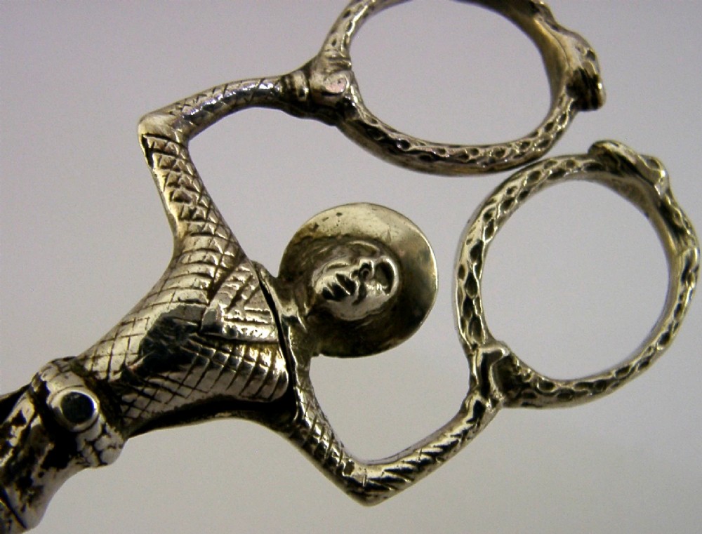 An Edwardian sterling silver sugar nip designed in the detailed shape of a harlequin jester with scissor-action handles and shell-shaped grips. View II