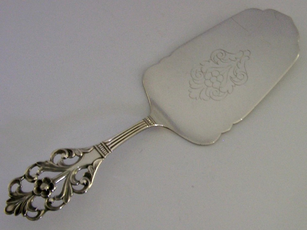 A Norwegian 830 solid silver cake server featuring an openwork scrollwork handle and an engraved floral pattern on the flat blade.