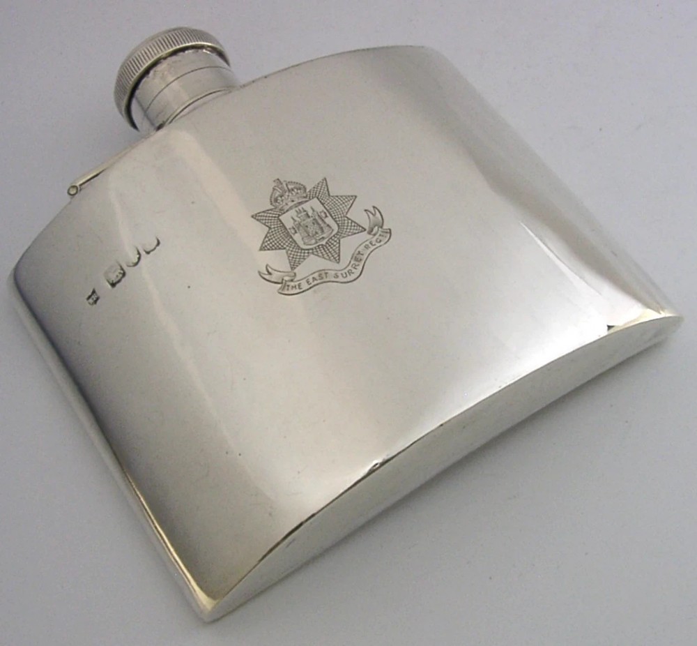 A curved sterling silver hip flask featuring an engraved East Surrey Regiment crest and clear British silver hallmarks.