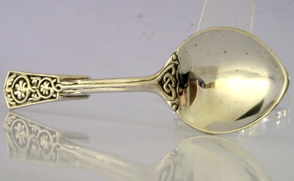 An English sterling silver honey spoon featuring a polished oval bowl, a hooked handle, and detailed Celtic knotwork decoration.