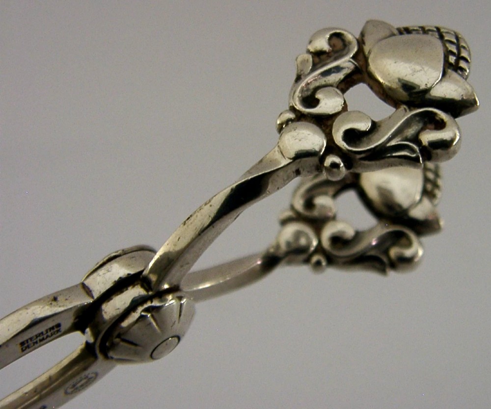 A pair of 1958 Georg Jensen sterling silver sugar tongs featuring the Acorn pattern handle design with central pivot joint and shell grips. View II