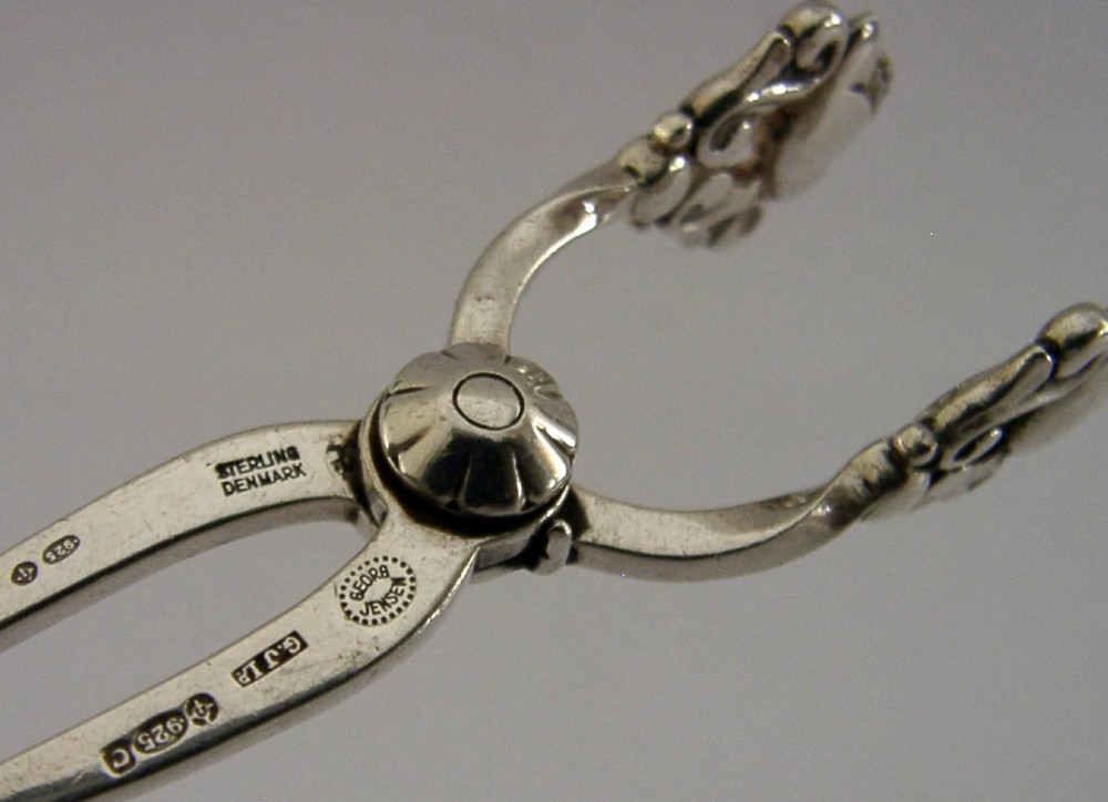A pair of 1958 Georg Jensen sterling silver sugar tongs featuring the Acorn pattern handle design with central pivot joint and shell grips. View III